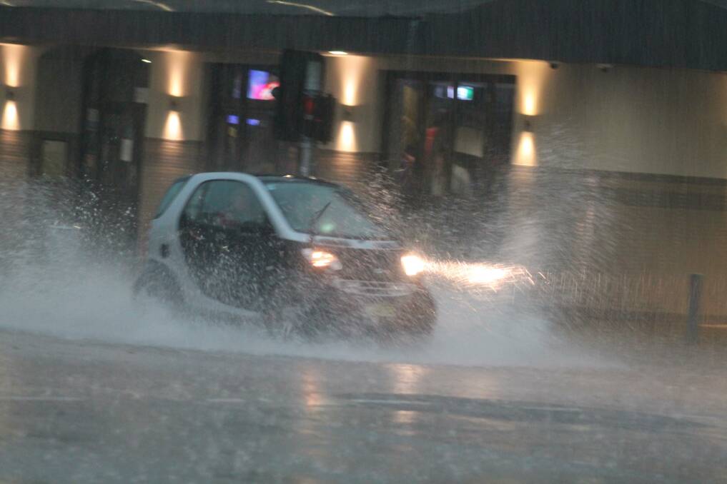 Cars drive through the rain on Monaro Street earlier this afternoon. 