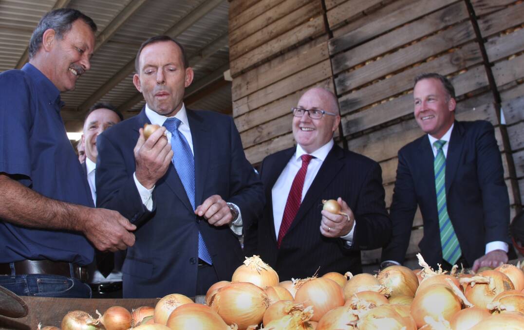 Then-prime minister Tony Abbott tries an onion at Charlton Farm Produce in 2015, watched by managing director David Addison (left) and fellow politicians Brett Whiteley and Will Hodgman. File picture