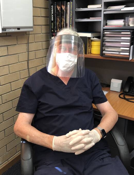 Dr Warwick Carter in his surgery, wearing face mask and gloves.
